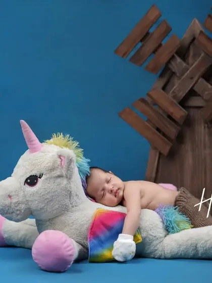 A magical moment with a mythical friend. Here, a sleeping baby rests peacefully on a large, soft unicorn plush, creating a whimsical and enchanting scene.