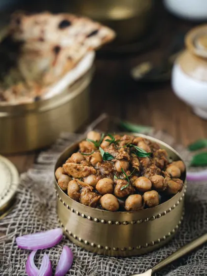 A rustic and moody shot of chole, served in a traditional brass bowl, perfect for pairing with hot naan or roti.