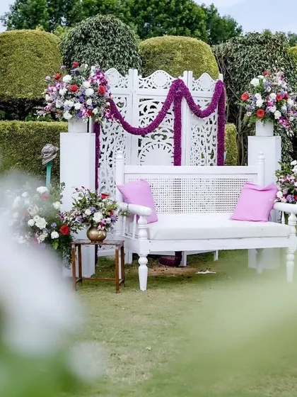 A dreamy Mehendi seating area with a white carved backdrop, floral arrangements, and pops of purple, creating an elegant garden party vibe.