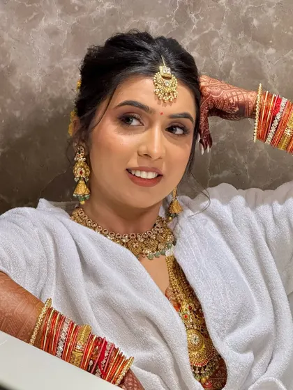 A candid shot of the bride getting ready, relaxed and happy in a bathrobe with her full jewelry and makeup on.