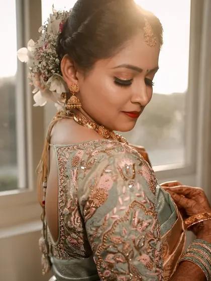 A bride looks over her shoulder, with soft sunlight highlighting the exquisite embroidery on her blouse. This portrait focuses on the beautiful details of the bridal outfit.
