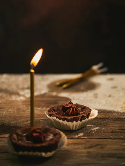 A moody shot of the chocolate tarts on a rustic wooden surface, with the candle flame as the main light source.