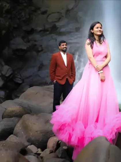 A stylish pre-wedding portrait featuring the bride in a vibrant pink gown, standing confidently in front of a beautiful waterfall, showcasing a blend of fashion and nature photography.