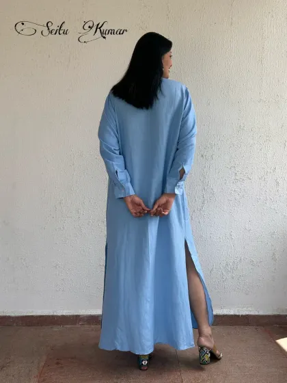 The back view of the long blue shirt dress, highlighting the side slits that add movement and a touch of allure.
