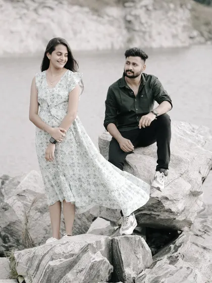 A relaxed and happy shot of a couple on rocks by a lake, the wind catching the bride's dress.