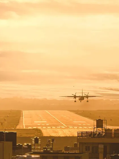An airplane makes its final approach for landing on a runway bathed in the warm, golden light of sunset. This image captures a beautiful moment in aviation and travel.
