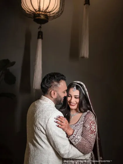 An intimate reception portrait, softly lit from above. The dark, moody background emphasizes the couple's bright smiles and the warmth of their interaction.