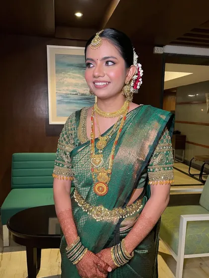 A full-length shot showing the bride's elegant posture and the beautiful drape of her saree. The makeup is soft and complements the traditional attire perfectly.