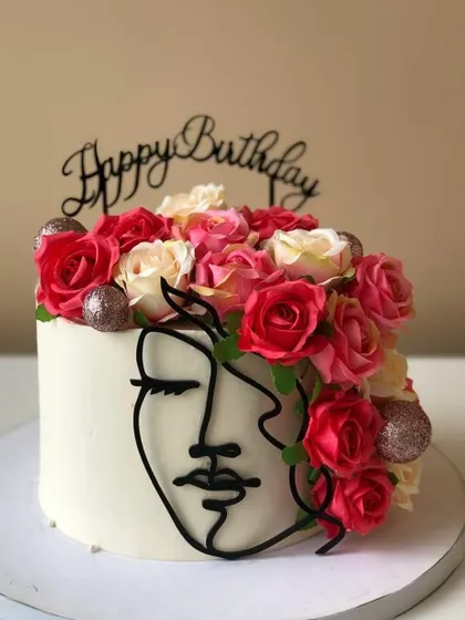 A modern and artistic cake featuring a line-art face and a crown of fresh roses. A beautiful centerpiece for a queen.