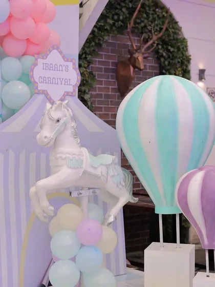 A delightful corner of a pastel carnival setup, featuring a carousel horse and hot air balloon props. The soft mint, purple, and pink colors create a dreamy and gentle atmosphere perfect for a first birthday.