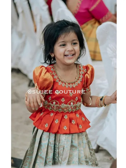 This is the beautiful Kanvi, smiling brightly in her custom-designed outfit. I created this special peplum blouse with traditional puff sleeves and intricate zardozi embroidery around the neckline and waist. It’s paired with a light, pleated lehenga skirt, making it perfect for her to run and play comfortably during any celebration.