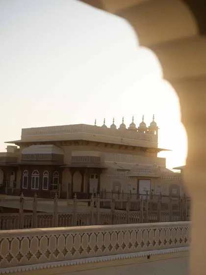 A view of the Chomu Palace at sunset, framed by an archway. This shot captures the romantic, golden-hour light that makes palace weddings in Rajasthan so magical.