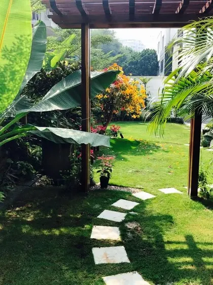 Where every step whispers tales of tranquility. This inviting garden entrance features a path of stone pavers leading through a wooden pergola, framed by large, lush tropical leaves.