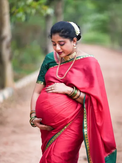 A beautiful portrait of an expecting mother in a traditional red and green silk saree, cradling her baby bump. We are experienced in capturing the grace and beauty of traditional maternity photoshoots.