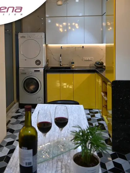 A contemporary kitchen with a pop of color. The bright yellow cabinets are balanced with white and black, and the geometric flooring adds a playful, modern touch. We also integrated the washing machine and dryer here.
