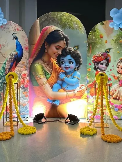 I design themed backdrops for religious and family functions. This setup for a Krishna-themed event features a custom printed backdrop of Yashoda and Krishna, framed by colorful balloon arches and marigold garlands.