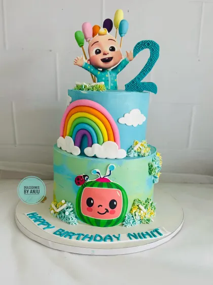 A two-tier Cocomelon cake featuring a big rainbow and cheerful character toppers.