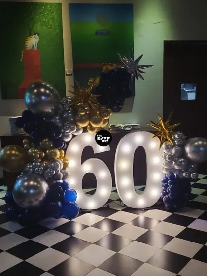 'Come Together' for a 60th birthday! This setup features a giant lit-up '60' and balloon arrangements on a classic black and white checkered floor.