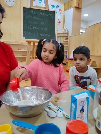 A child carefully pours milk into the mixing bowl. Activities involving pouring help develop a steady hand and fine motor control, skills that are essential for writing.