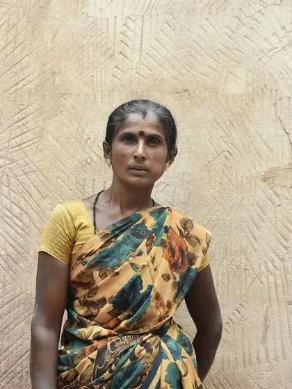 Portrait of Saroja, a quiet and steady woman mason, against a textured Thappi plaster wall. Her work speaks volumes about her skill and dedication.