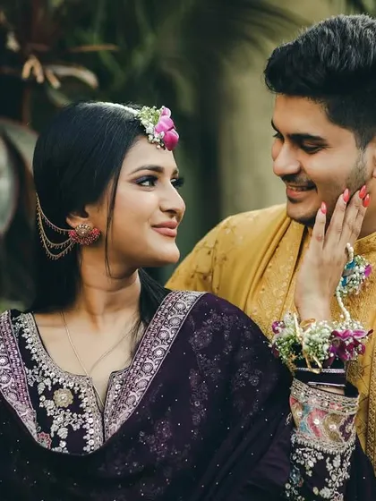 A sweet, candid moment from a Haldi ceremony. The bride gently touches the groom's face, their expressions full of affection and playfulness, highlighted by their colorful, traditional attire.
