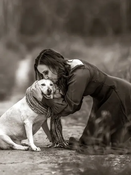 A deeply emotional black and white portrait of a woman sharing a tender kiss with her dog. This image captures the profound, unconditional love between a human and her pet.
