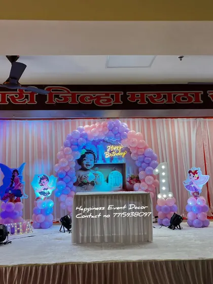 This fairy-themed stage decor uses a balloon arch and multiple fairy cutouts to create a magical wonderland for a first birthday party.