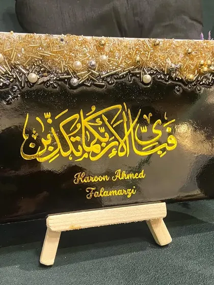 A personalized tabletop plaque featuring the verse from Surah Ar-Rahman. The black resin base makes the gold calligraphy and textured embellishments pop, creating a striking decor item.