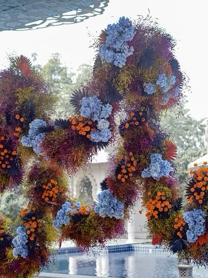 A stunning, cloud-like floral installation suspended over a pool. This piece, made from thousands of flowers in shades of blue, orange, and deep red, was the artistic centerpiece of the 'Azure Ochre' event.