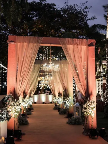 An elegant and sophisticated entrance with soft peach drapes, chandeliers, and white floral arrangements.