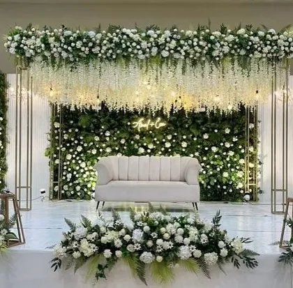 For a sophisticated engagement or reception, nothing beats a classic white and green theme. This stage features a lush green wall covered in white roses, with hanging wisteria flowers and a custom neon sign, creating an elegant and romantic setting.