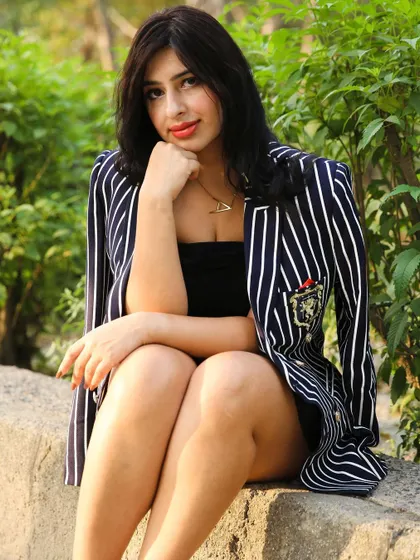 A relaxed, seated portrait from an outdoor shoot, showcasing a chic and preppy look with a striped blazer.