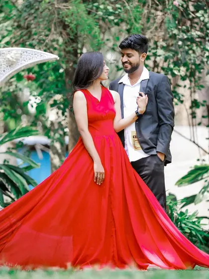 A romantic pre-wedding photo by a crescent moon prop, with the long trail of the red dress spread out on the grass.
