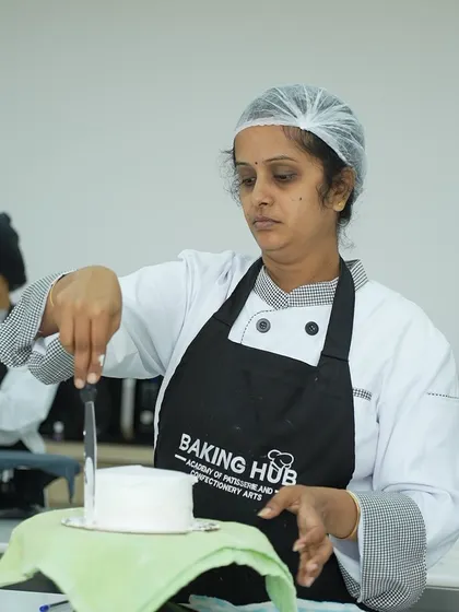 Precision is key. A student uses a palette knife to level the top of her cake, ensuring a flat and even surface before applying fondant. We focus on these foundational details from day one.