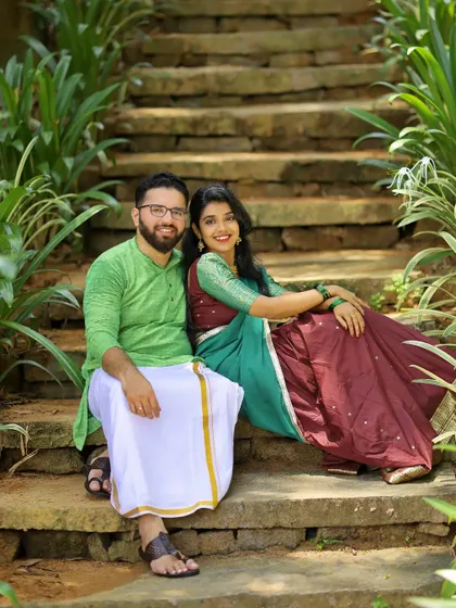 A sweet portrait of a couple sitting on stone steps in a garden, dressed in traditional South Indian attire for their pre-wedding shoot.