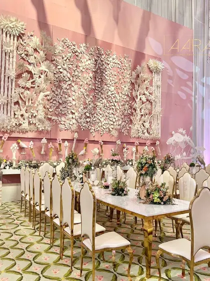 An incredible family dining experience set against an intricately crafted pith wall. The long marble tables are paired with elegant gold and cream chairs, while the floral centerpieces add a touch of softness to the grand setting.