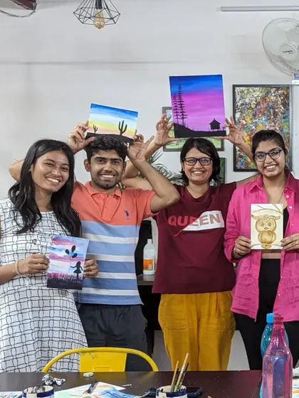 A group of friends proudly holding up their finished coffee and watercolor paintings.