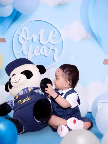 A one-year-old boy plays with a teddy bear in a custom-designed blue hot air balloon themed set.