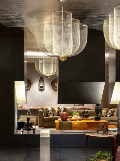 The formal living room is designed around a central fireplace, with its structure in brass and honed granite. The large mesh lights create a dramatic effect, reflected in the room's mirrored surfaces.