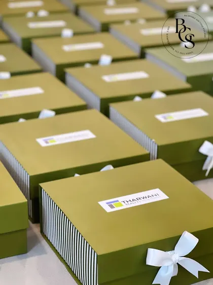 An example of branded corporate gifting. These olive green and white striped boxes feature the client's logo, "Tharwani Realty," prominently on the lid, and are finished with a clean white bow for a professional look.
