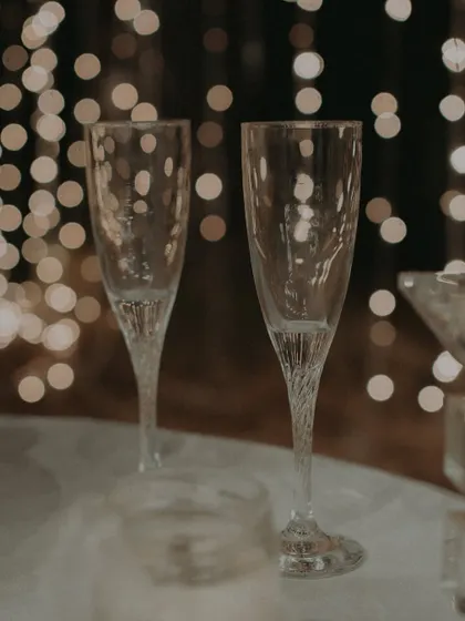 An atmospheric detail shot of two empty champagne flutes against a bokeh background of fairy lights.