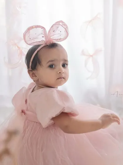 A whimsical first birthday portrait with floating pink bows. The creative setup and the baby's curious glance back make this a unique and magical image.