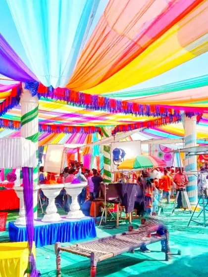 This is a large-scale Holi party pandal I decorated. I used vibrant, multi-colored fabric drapes across the ceiling and arranged traditional charpai seating to create a lively and authentic desi celebration space for the community.