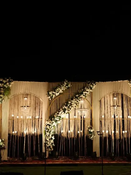 We used warm lighting and cascading floral arrangements to create this romantic reception stage. The combination of delicate string lights and white flowers against a draped backdrop set a cozy and inviting mood.