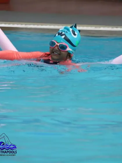 A happy swimmer uses a pool noodle for buoyancy support while practicing. Flotation aids are used to help beginners focus on their stroke mechanics without worrying about staying afloat.