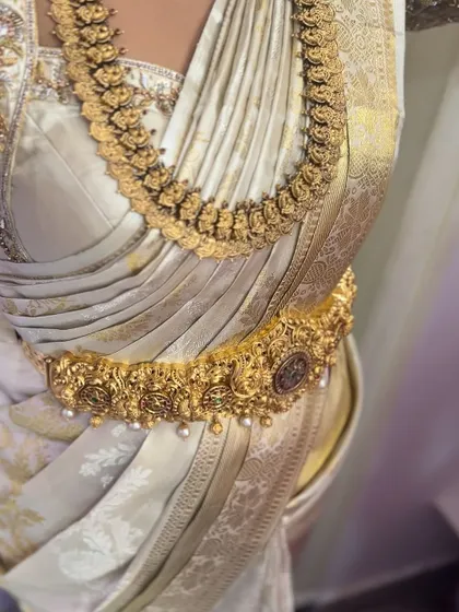 A close-up on a white silk saree, showing the clean lines of the drape. The pleats are perfectly aligned, creating a look of effortless elegance.