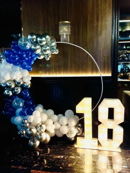 An 18th birthday party setup with a blue, white, and silver balloon arch and marquee numbers.