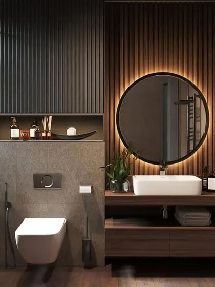 This bathroom design plays with textures, combining fluted dark panels, a concrete-finish wall, and wood flooring. The round back-lit mirror softens the look and provides excellent lighting.