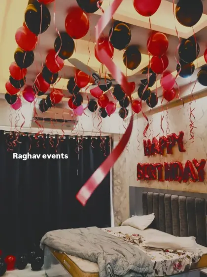 A red and black themed birthday room decoration. The ceiling is filled with balloons, and 'Happy Birthday' foil letters are placed on the wall above the bed.