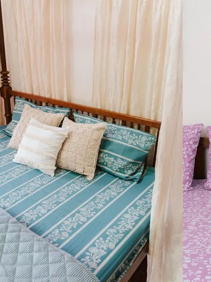 A glimpse of two different bedroom styles. On the left, a four-poster bed dressed in our teal 'Rani' collection bedsheet, and on the right, a bed with our lilac 'Cherry Blossom' print. Both show the versatility of our designs.